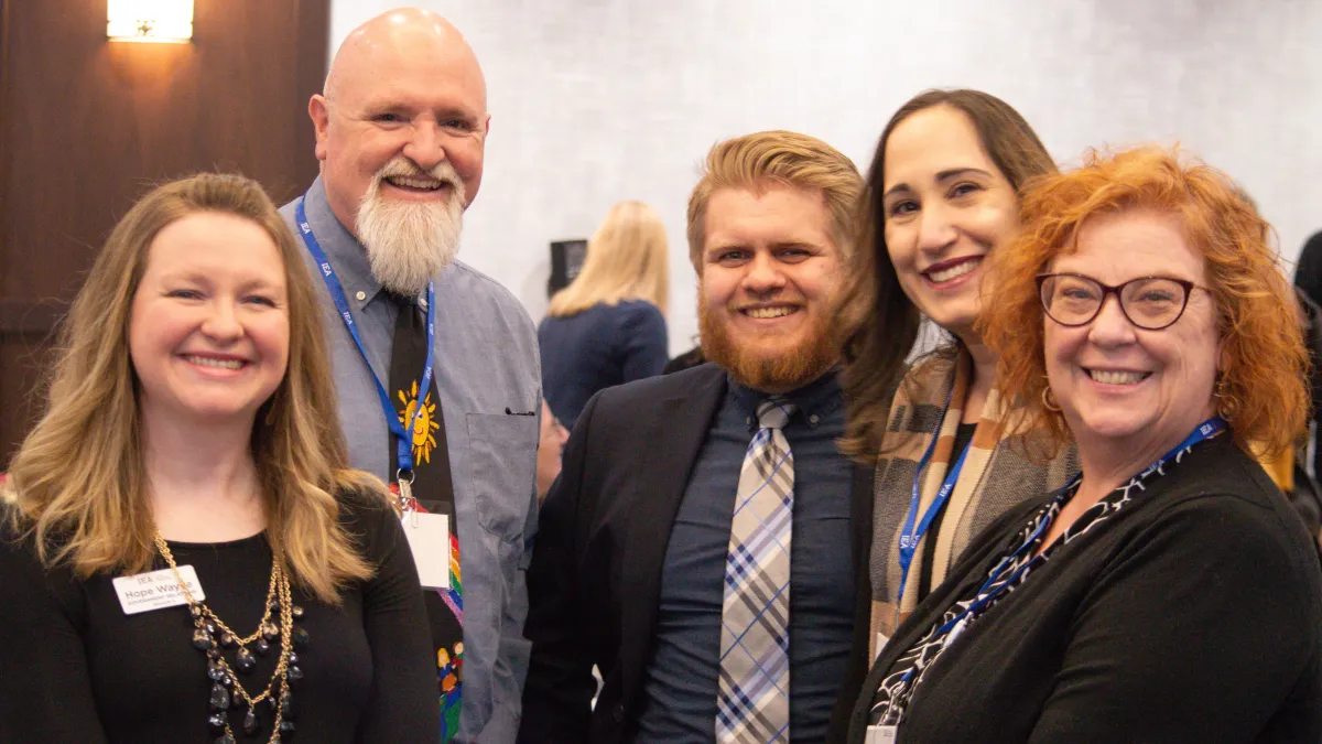 Group of three women and two men in professional dress, looking at camera and smiling