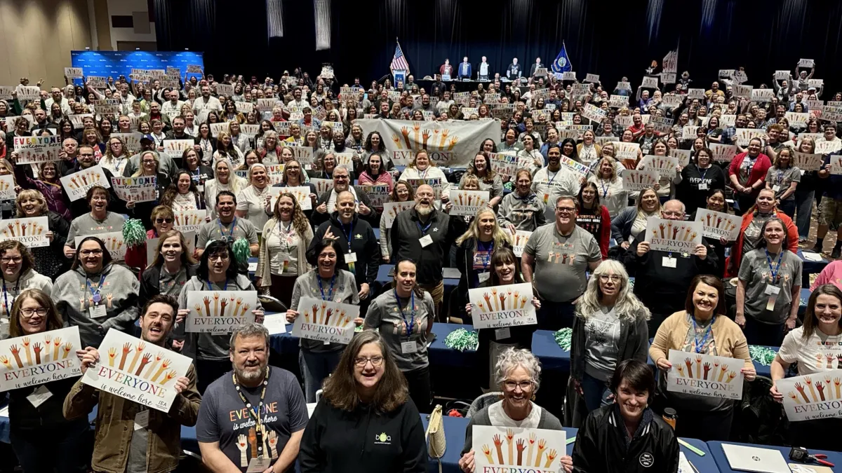 Delegates at 2025 Delegate Assembly holding up everyone is welcome here signs