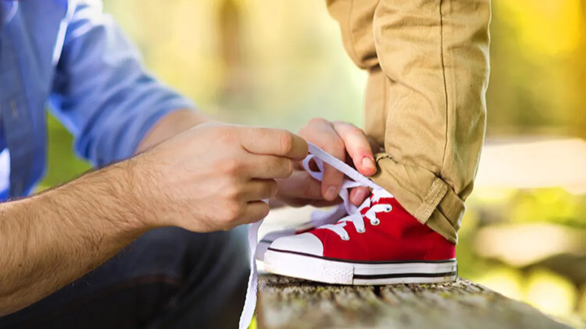 man in blue shirt tying child's red shoes
