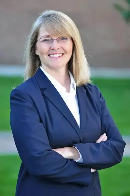 A photo of a woman with blonde hair and glasses wearing a blue suit