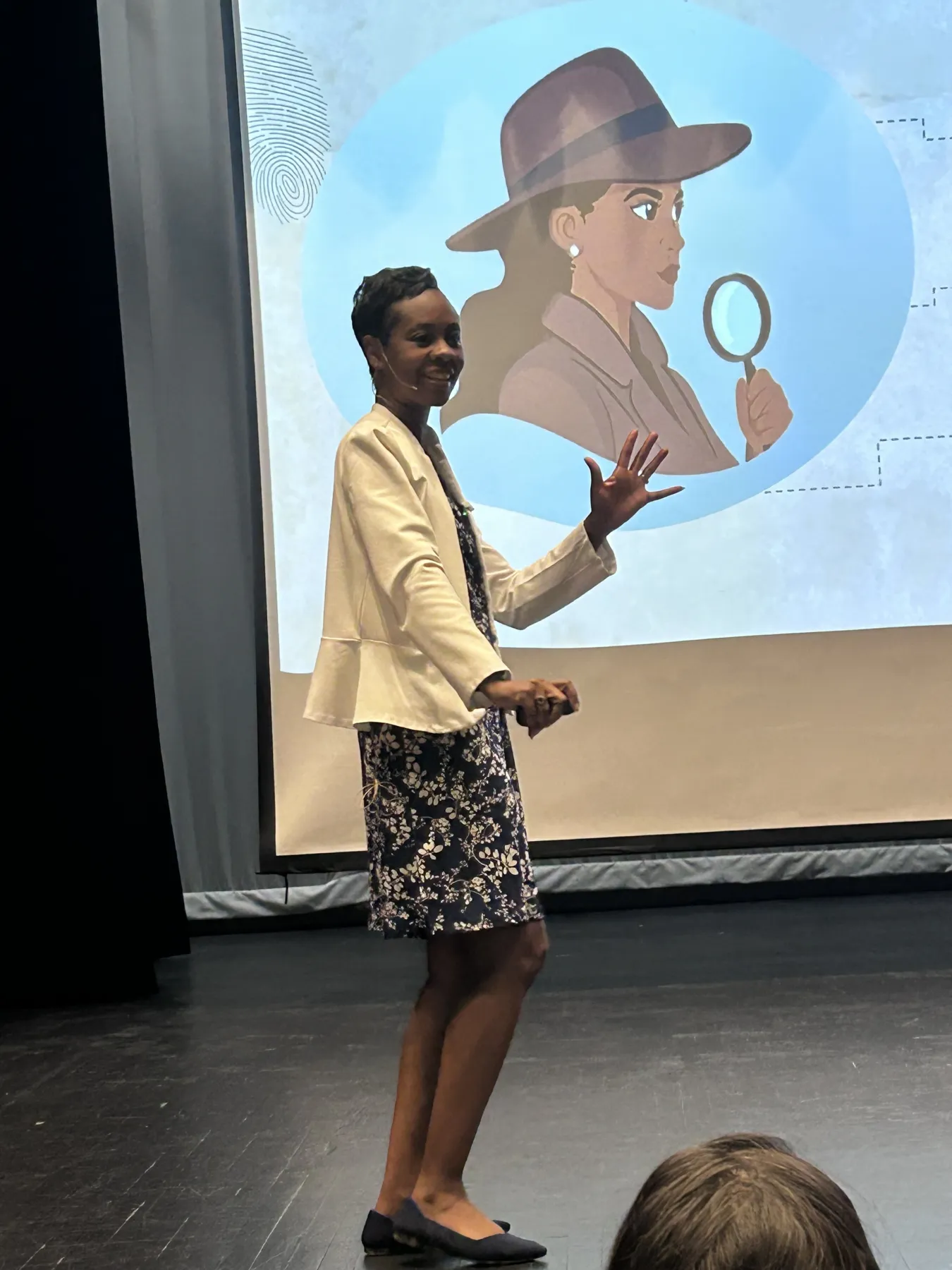 A woman stands on a stage in front of an avatar of a detective