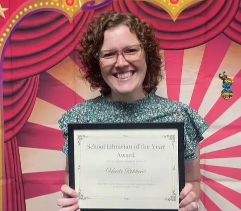 A woman smiles while holding a certificate against a colorful backdrop