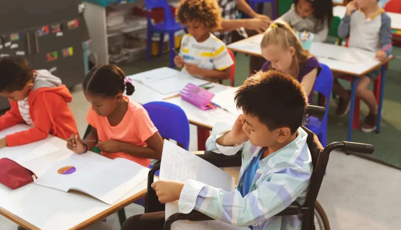 A child in a wheelchair studies alongside other children
