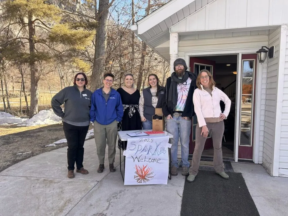 A group of people in front of a white house with a sign that says 2025 Sparks Welcome