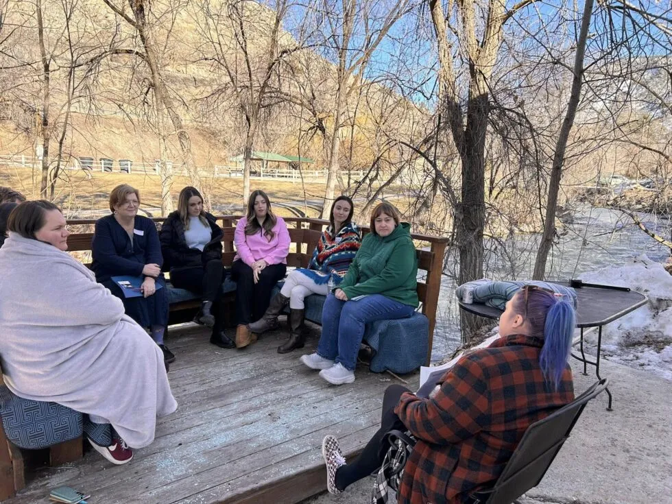 A group of people sitting outside, wearing coats and blankets