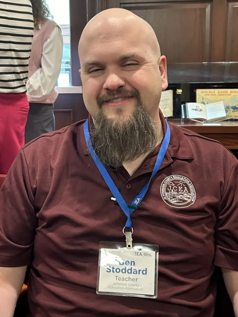A man with a goatee and a maroon shirt smiles at the camera