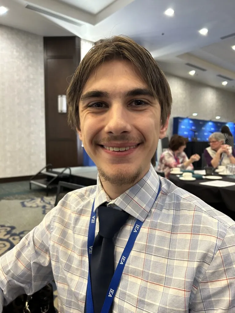 A man wearing a black tied and checked shirt smiles at the camera