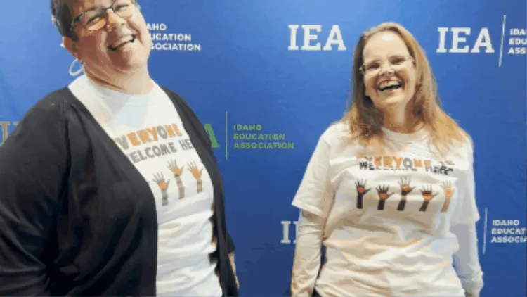 Two women wearing Everyone is Welcome Here shirts laughing and embracing