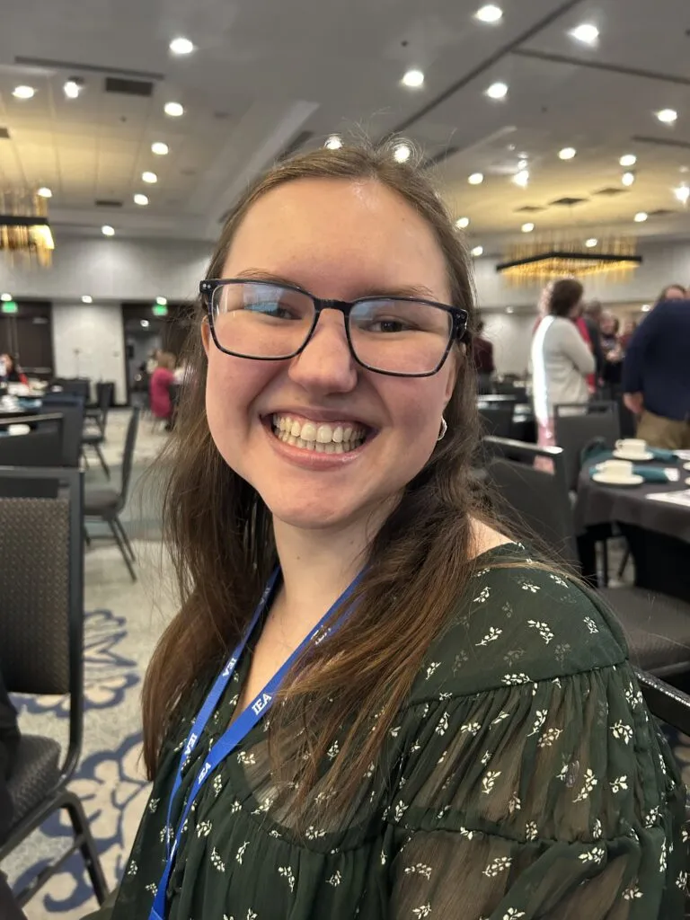 A woman with glasses and a green shirt smiles at the camera