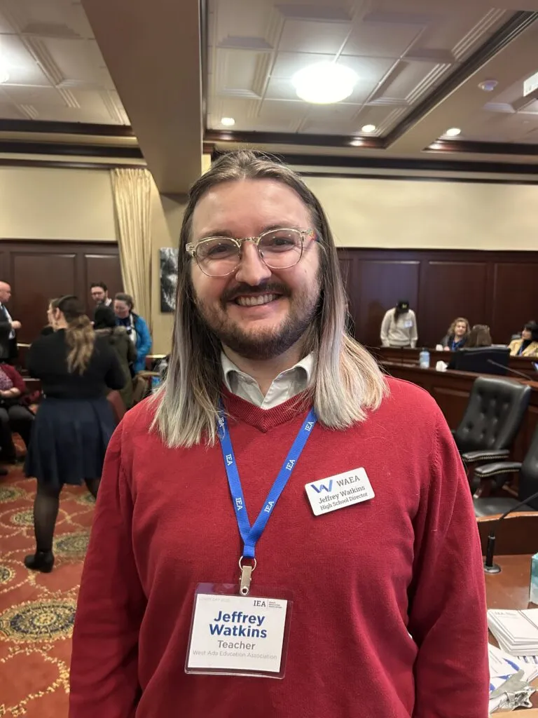 A man with glasses and a red sweater smiles at the camera