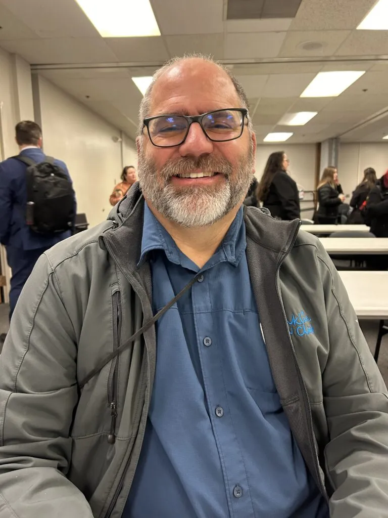 A man with a beard and glasses smiles at the camera