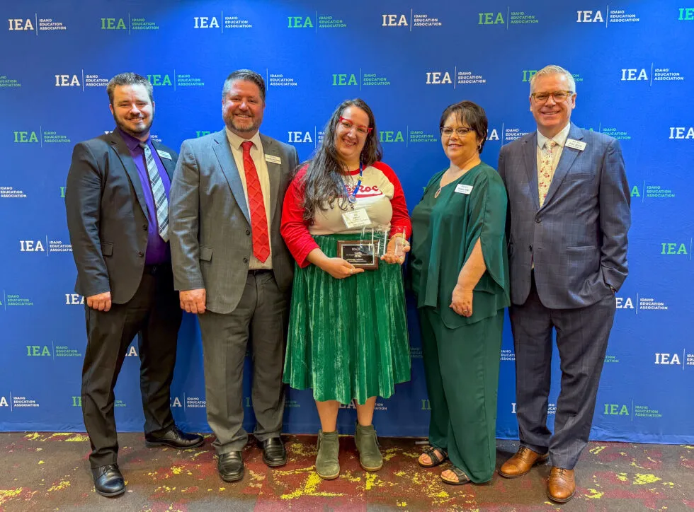 A woman wearing a green skirt and holding an award is surrounded by smiling people