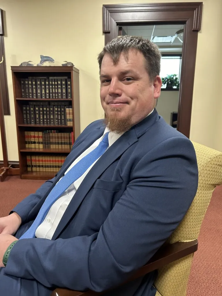 A seated man in a blue suit smiles at the camera