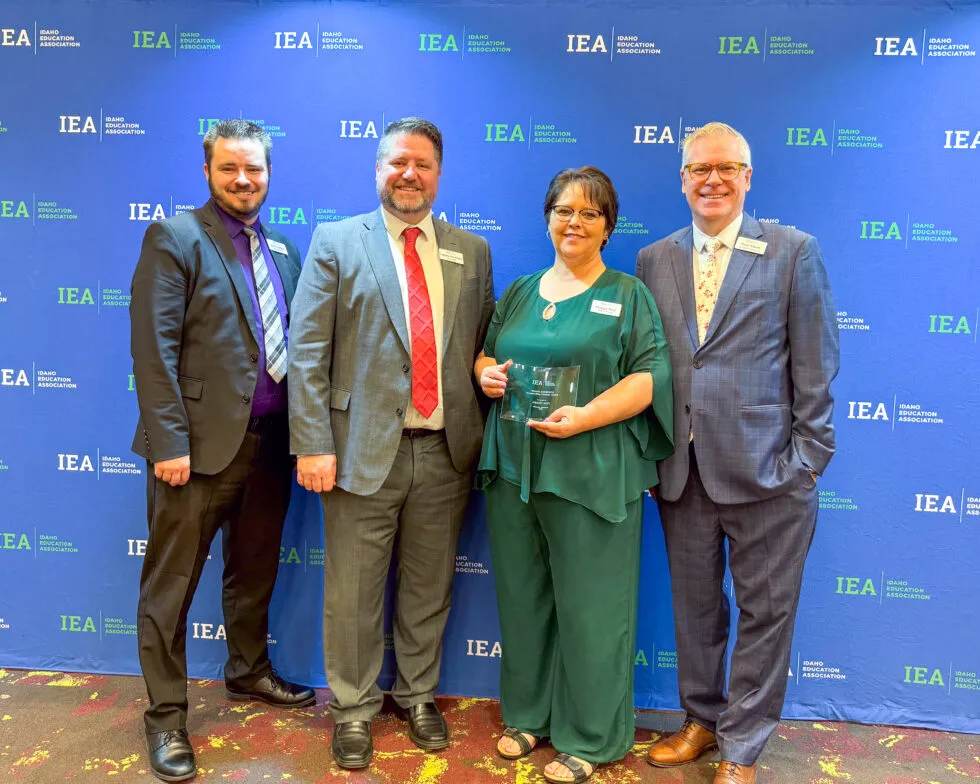 A woman in green holds an award surrounded by three men