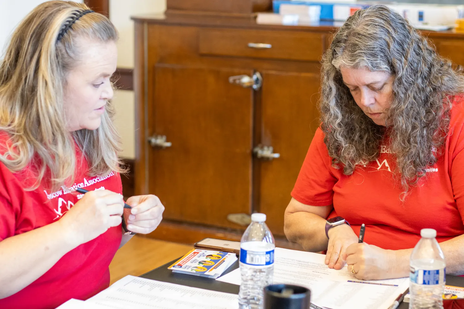 Two women in red t-shirts address postcards to voters. 