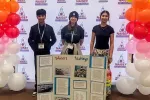 A group of three smiling students pose behind a science project