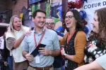 A smiling man in a blue shirt surrounded by laughing and yelling colleagues