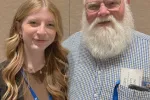 A young woman with blonde hair and an older man with a white beard pose together