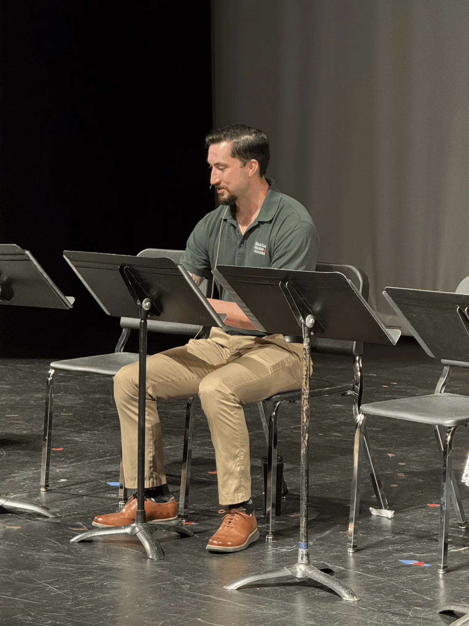A man sits on a stage and reads from papers in front of him