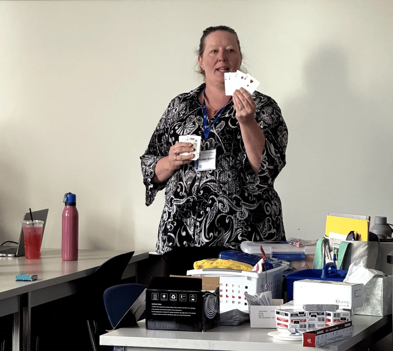 A woman stands in front of a class and displays playing cards