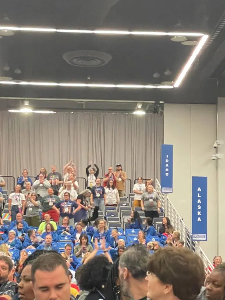 A group of people in a crowd stand up and cheer