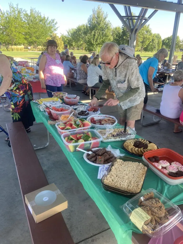 Retired people browse potluck offerings on a picnic table