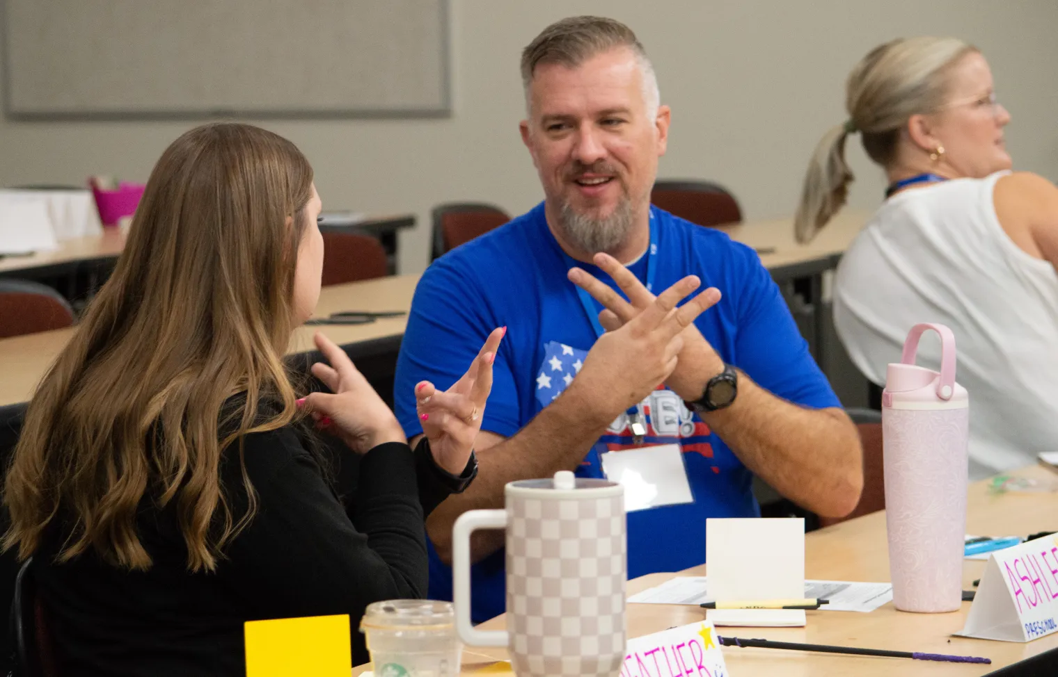 A man in a blue shirt practices American Sign Language with a woman in a black shirt