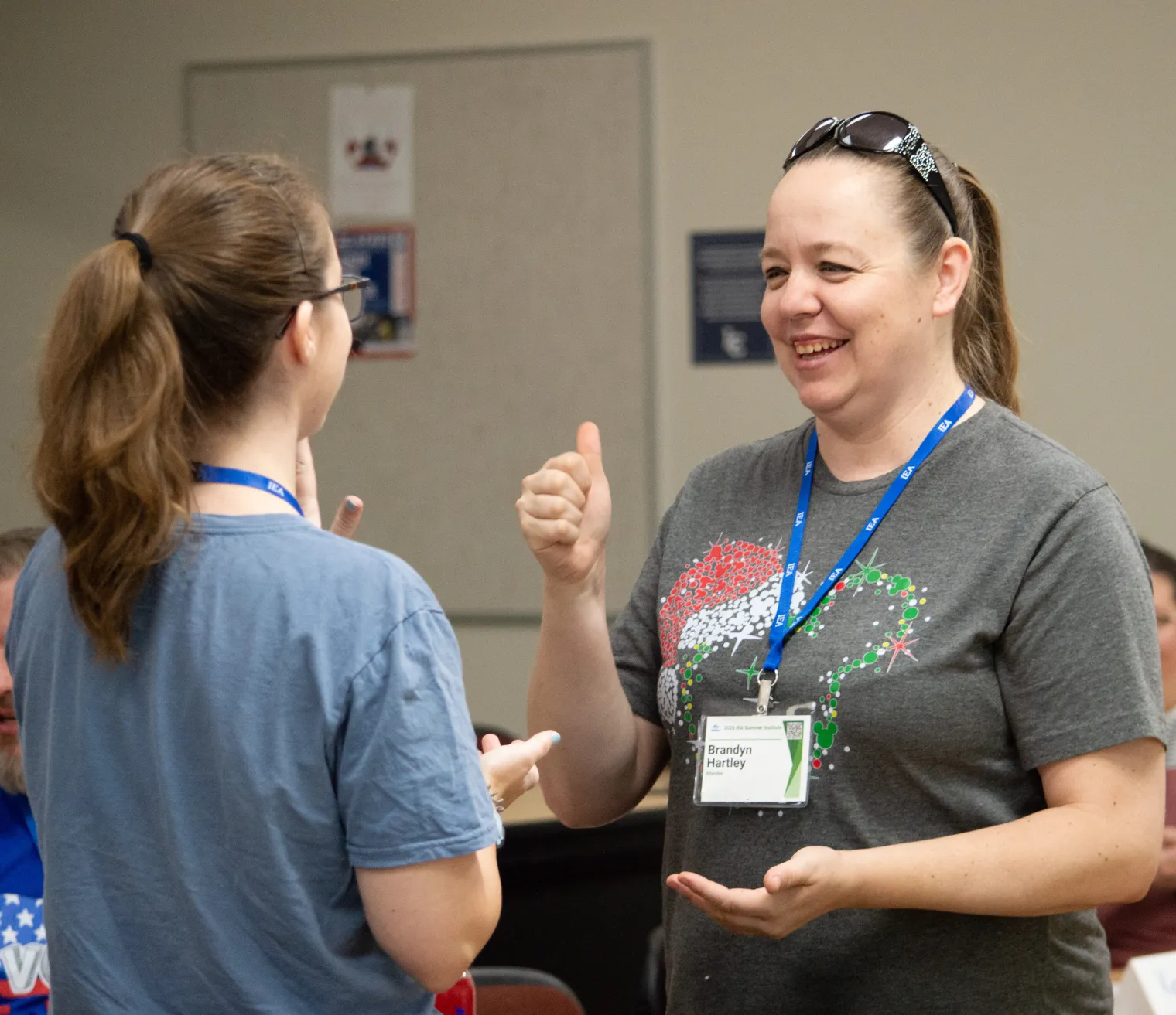 A woman in a gray shirt uses American Sign Language to speak to a woman in a blue shirt
