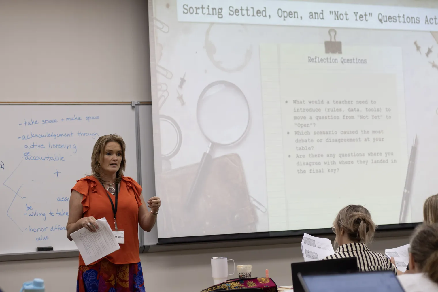 A woman in an orange shirt speaks in front of a class