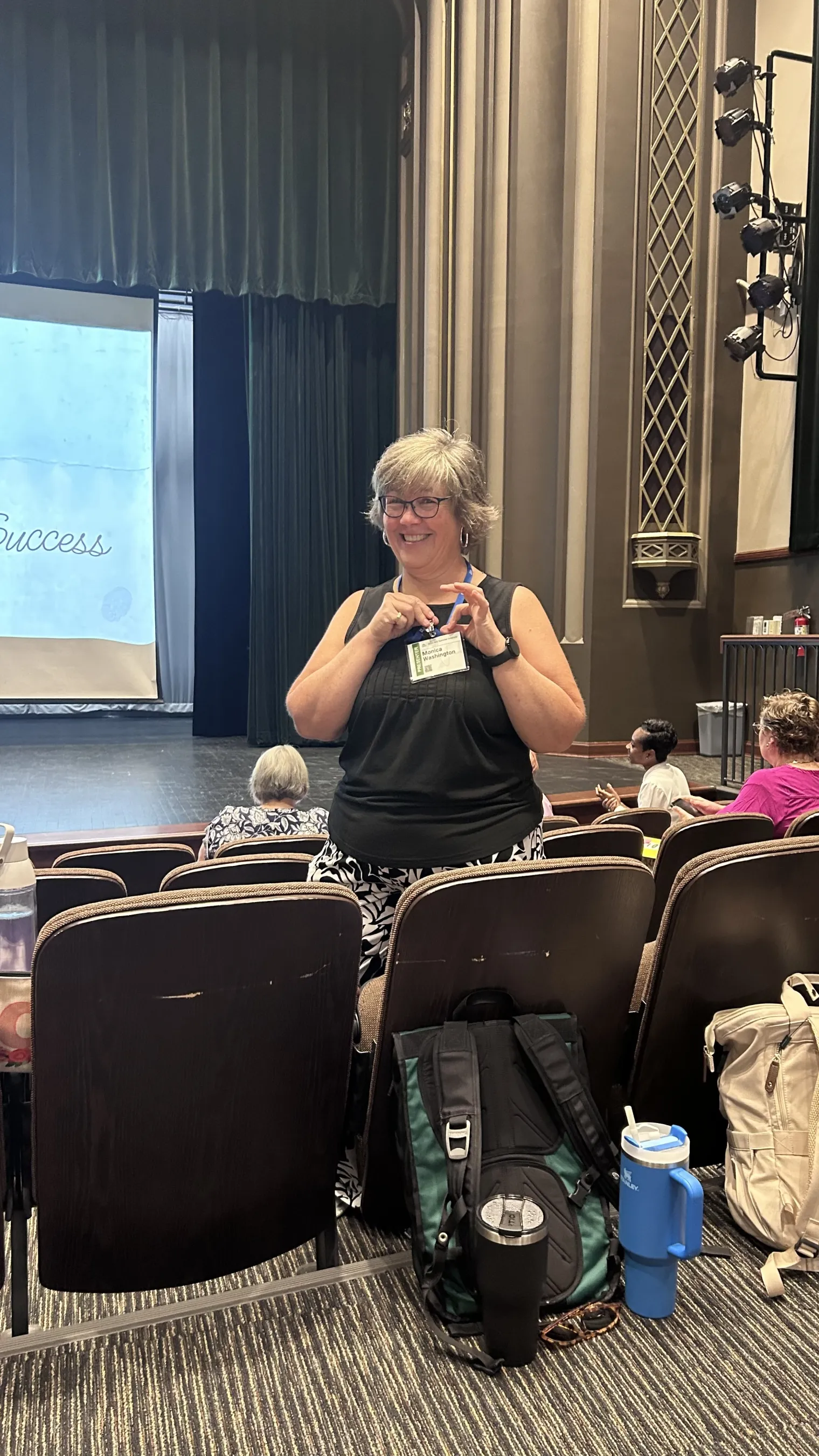 A woman in a black shirt stands among theater seats