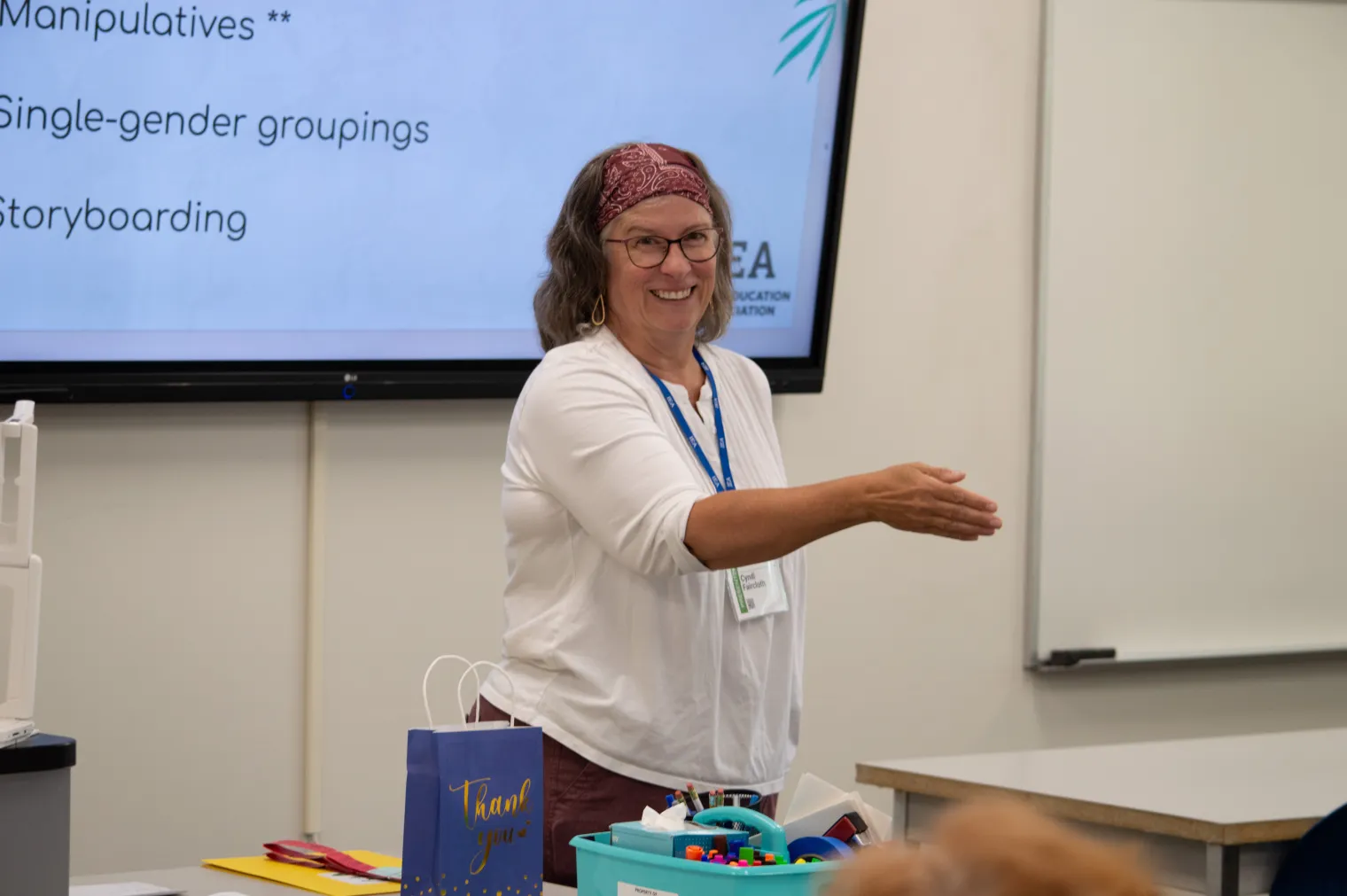 A woman in a white shirt and red bandanna gestures at a class