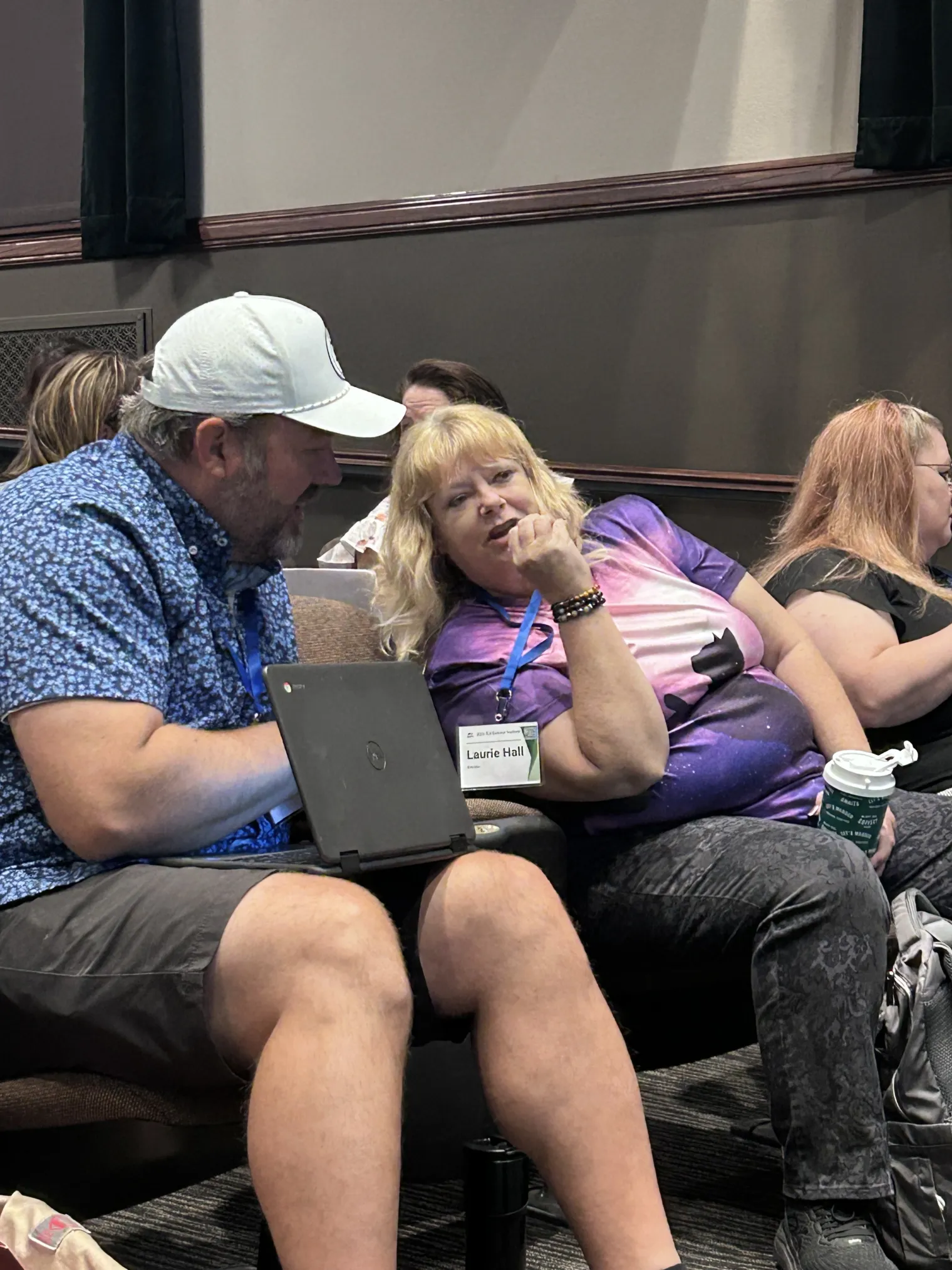 A woman leans over to speak to a man in a crowded theater