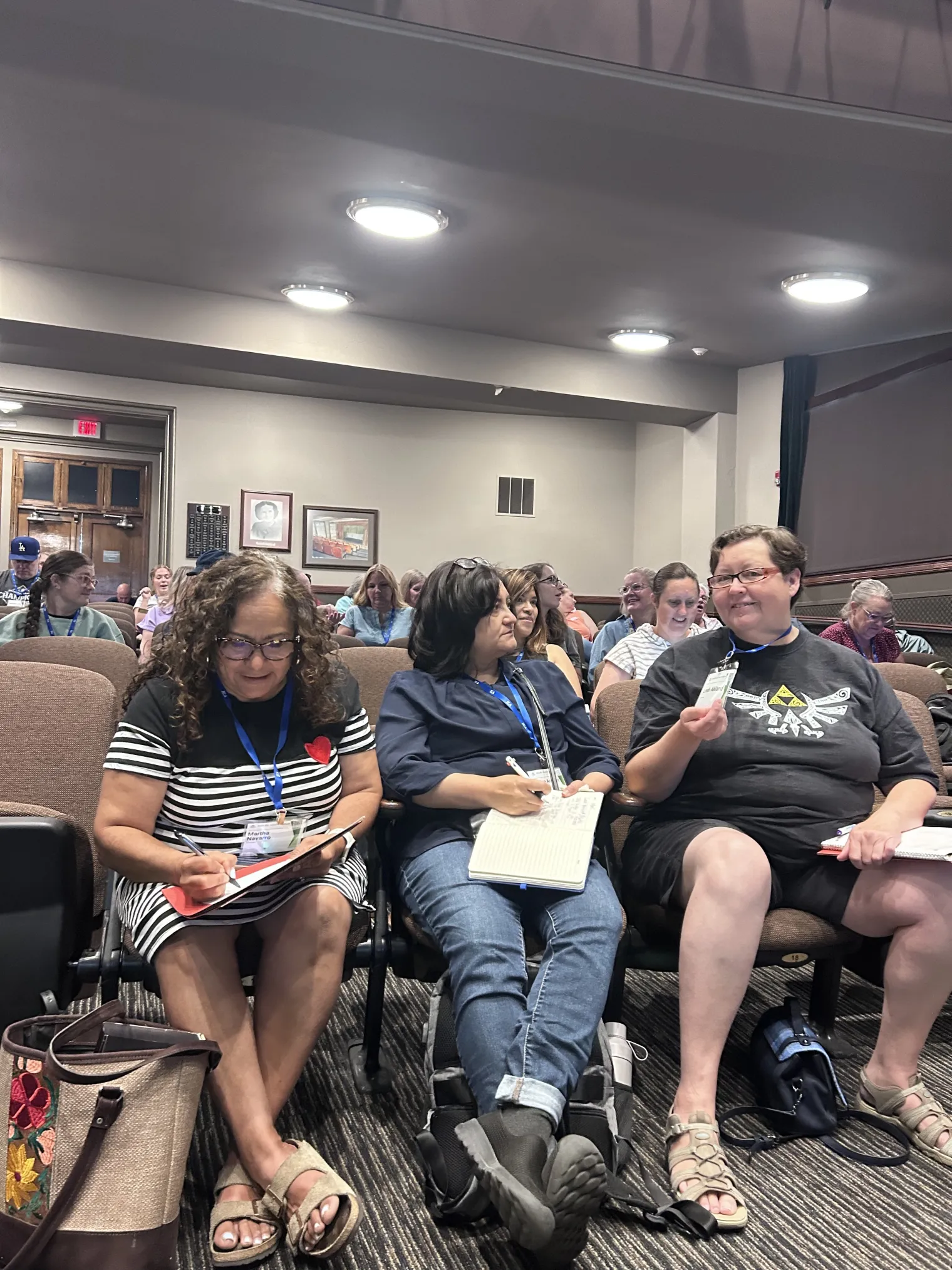 Three people in auditorium seats hold papers and speak to each other