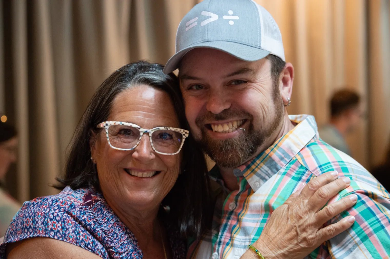A woman with glasses and a man in a baseball cap embrace