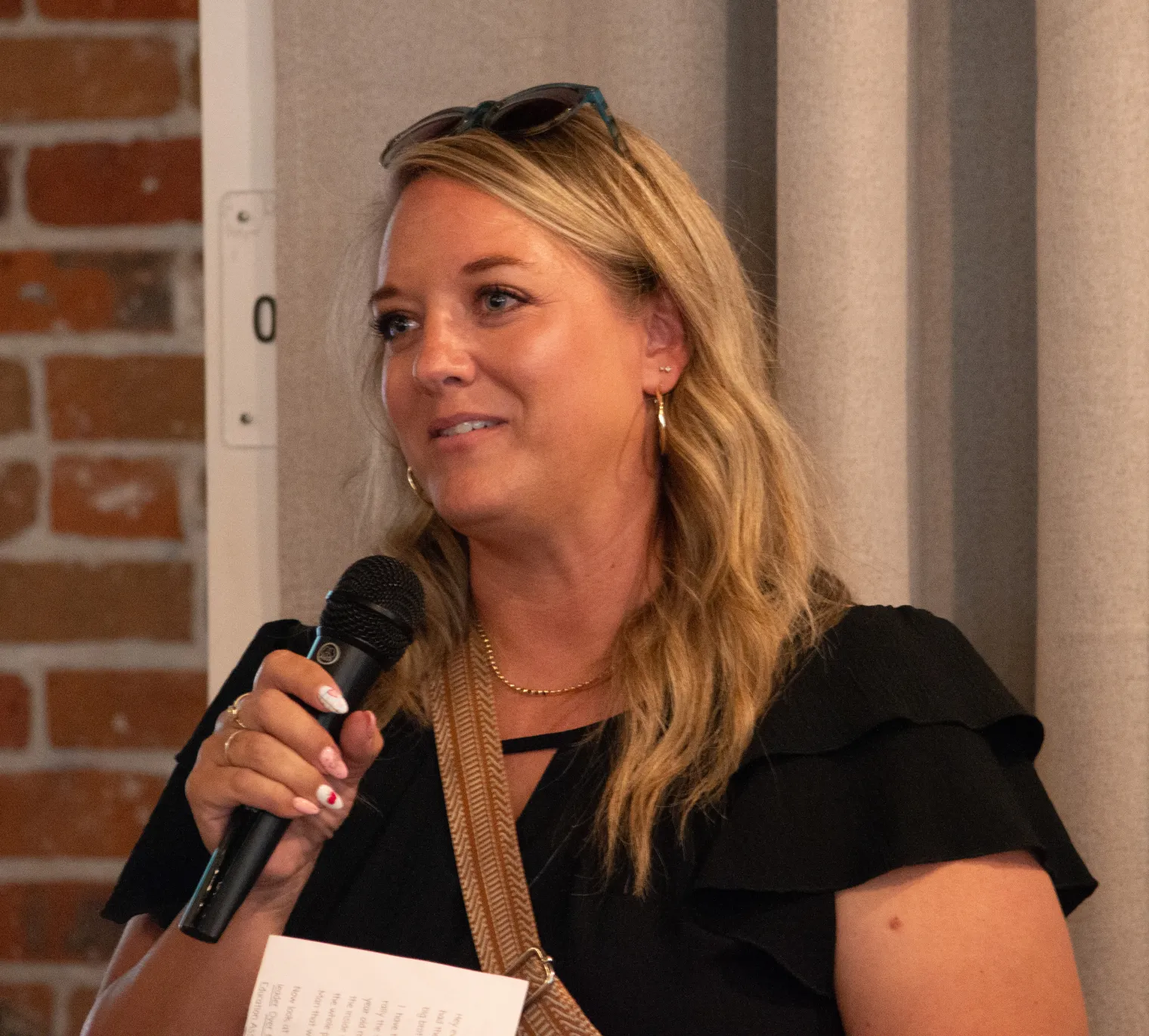 A woman with blonde hair holds a microphone and speaks