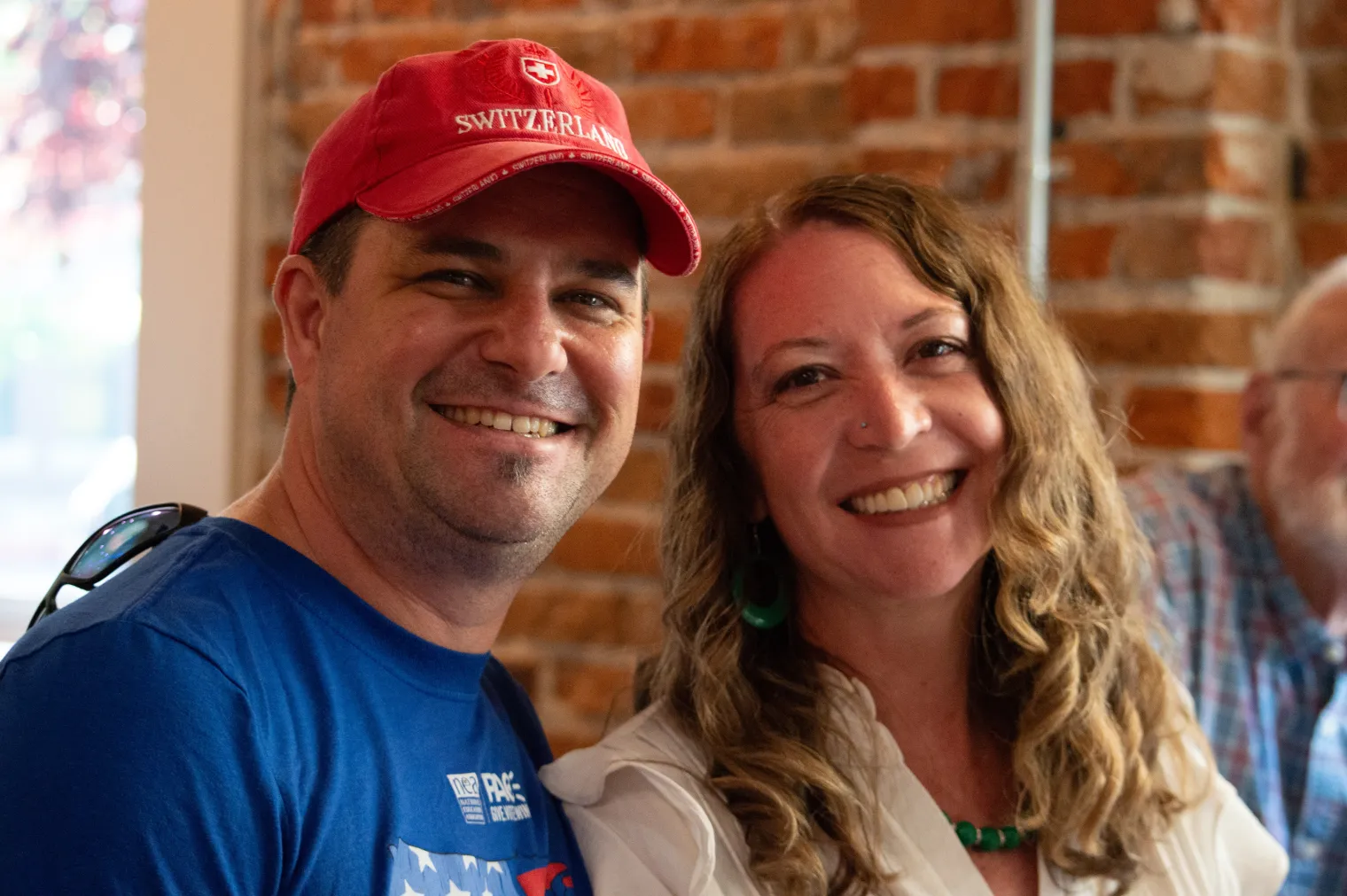 A man in a red baseball cap and blue shirt smiles next to a woman with a white shirt