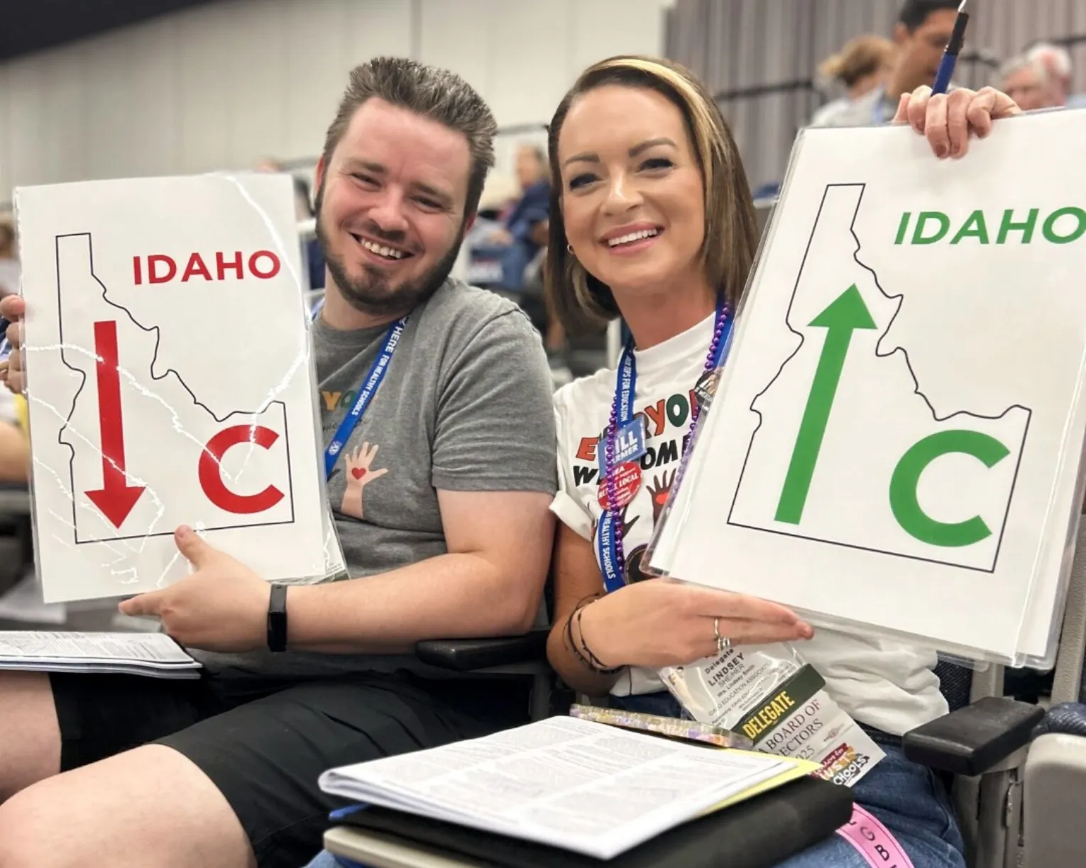 Two IEA delegates at the 2025 NEA RA show the IEA caucus position signs for NBIs being debated.