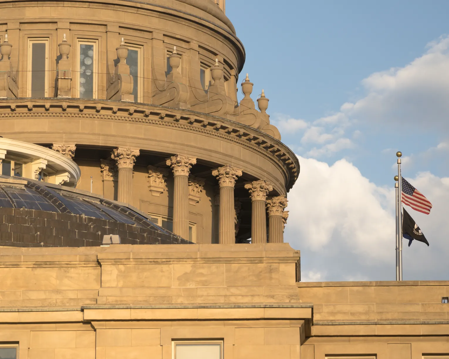 A zoomed in photo of the Idaho State Capitol with clouds in the background. 