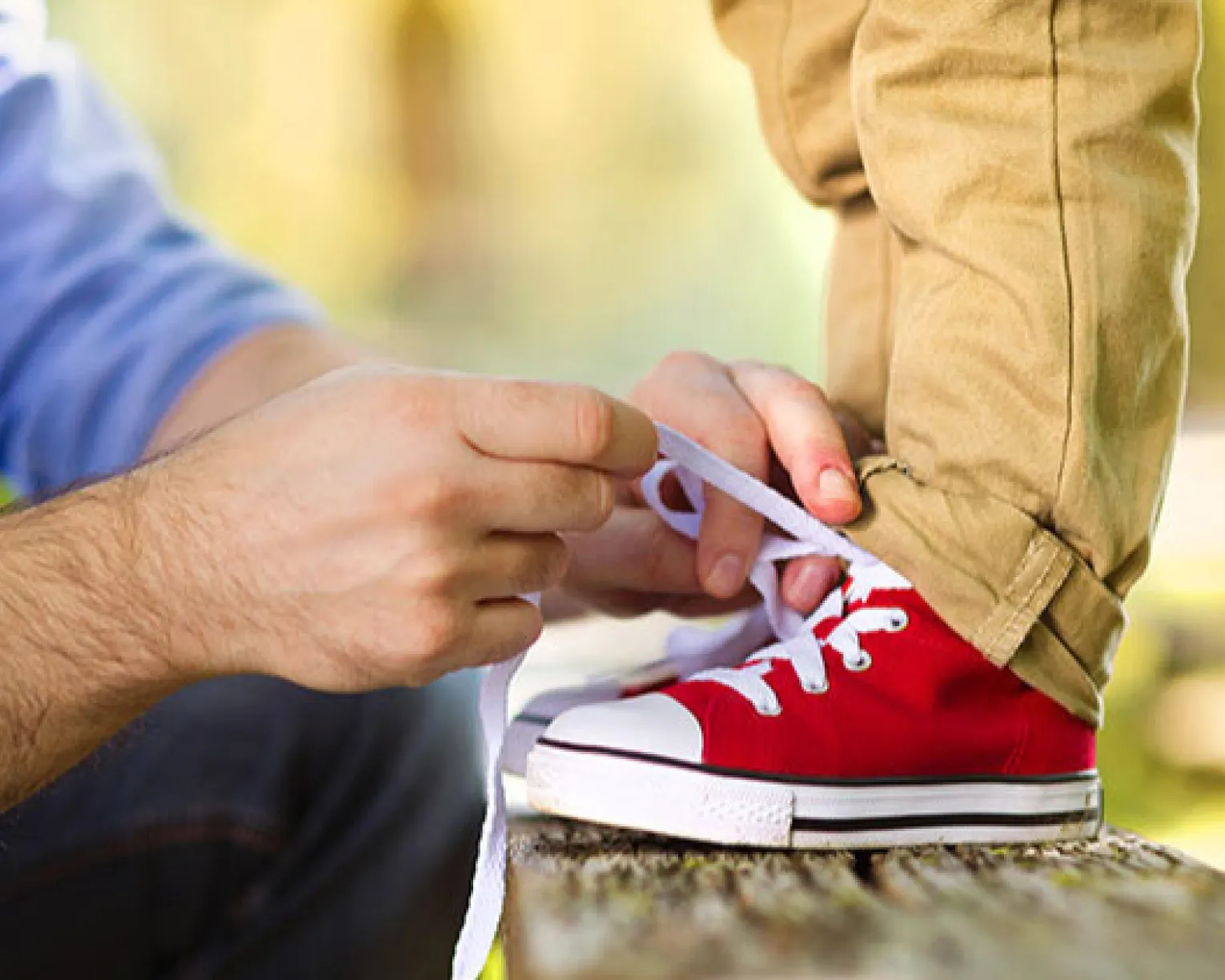 man in blue shirt tying child's red shoes