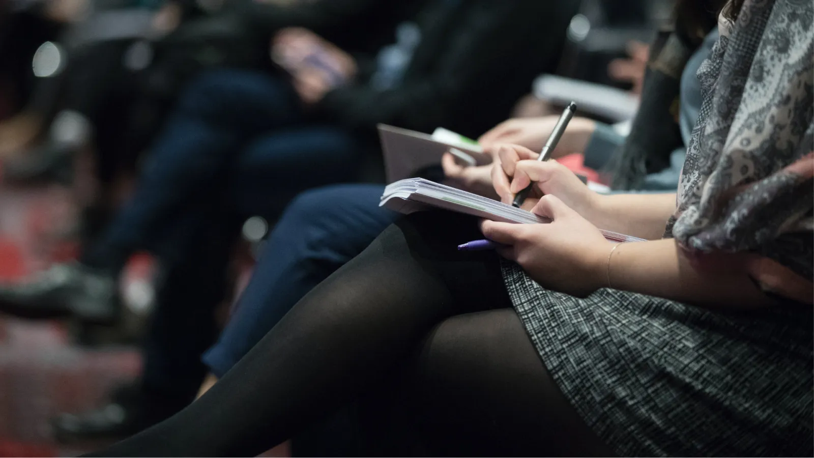 A shot of a group of reporters sitting in crowd taking notes