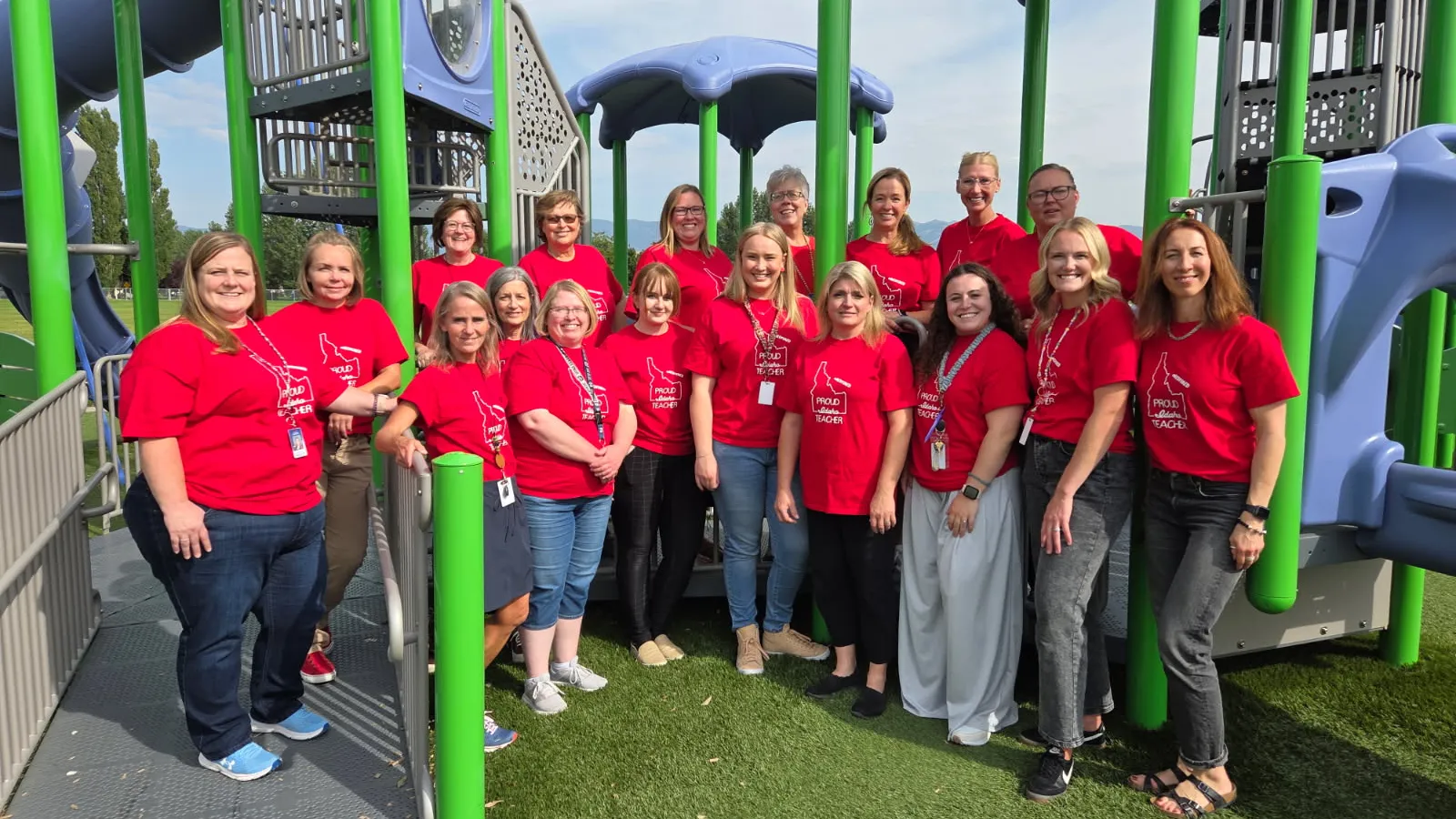 A group of people wearing red shirts poses beneath playground equipment