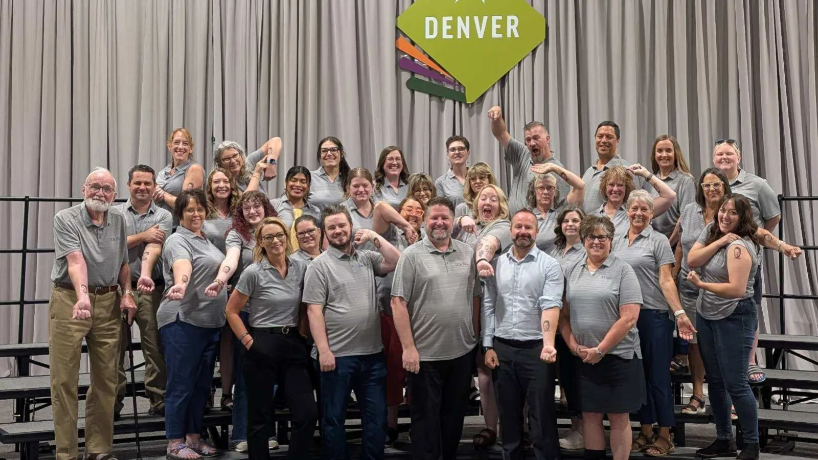 A group of people in gray shirts in front of a sign that says Denver