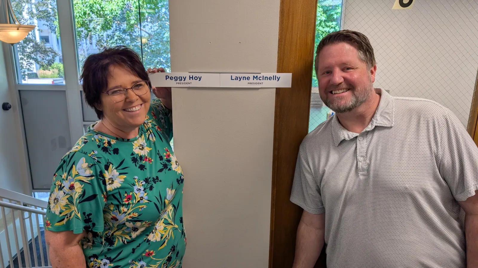 A man and a woman stand next to their office nameplates