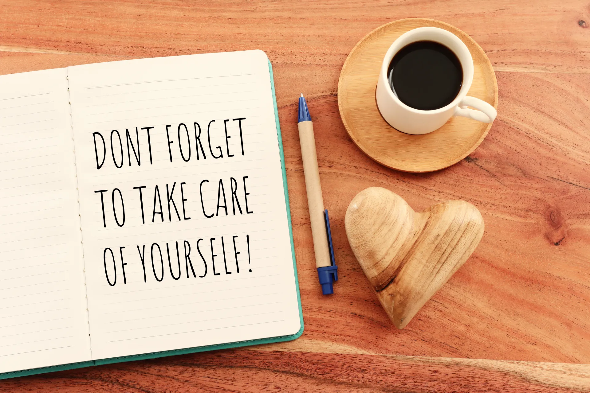 A cup of coffee and an open notebook with a page that says "Don't forget to take care of yourself!" 