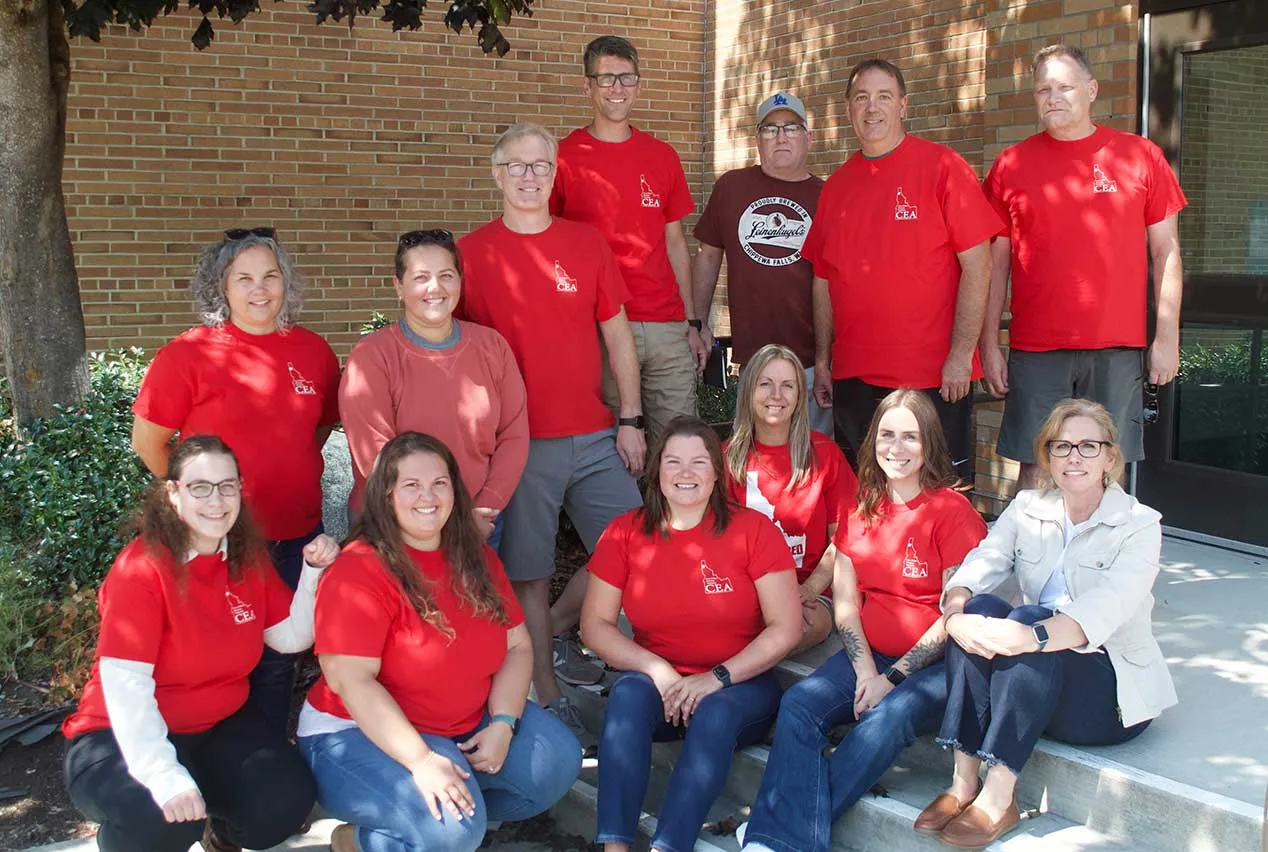 A group of smiling people wearing red shirts pose beneath a tree