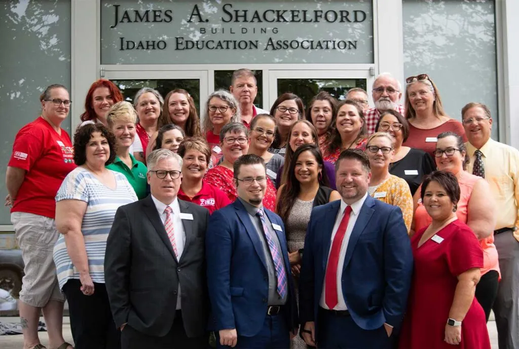 A group of people, mostly wearing red, standing outside a building a smiling at the camera
