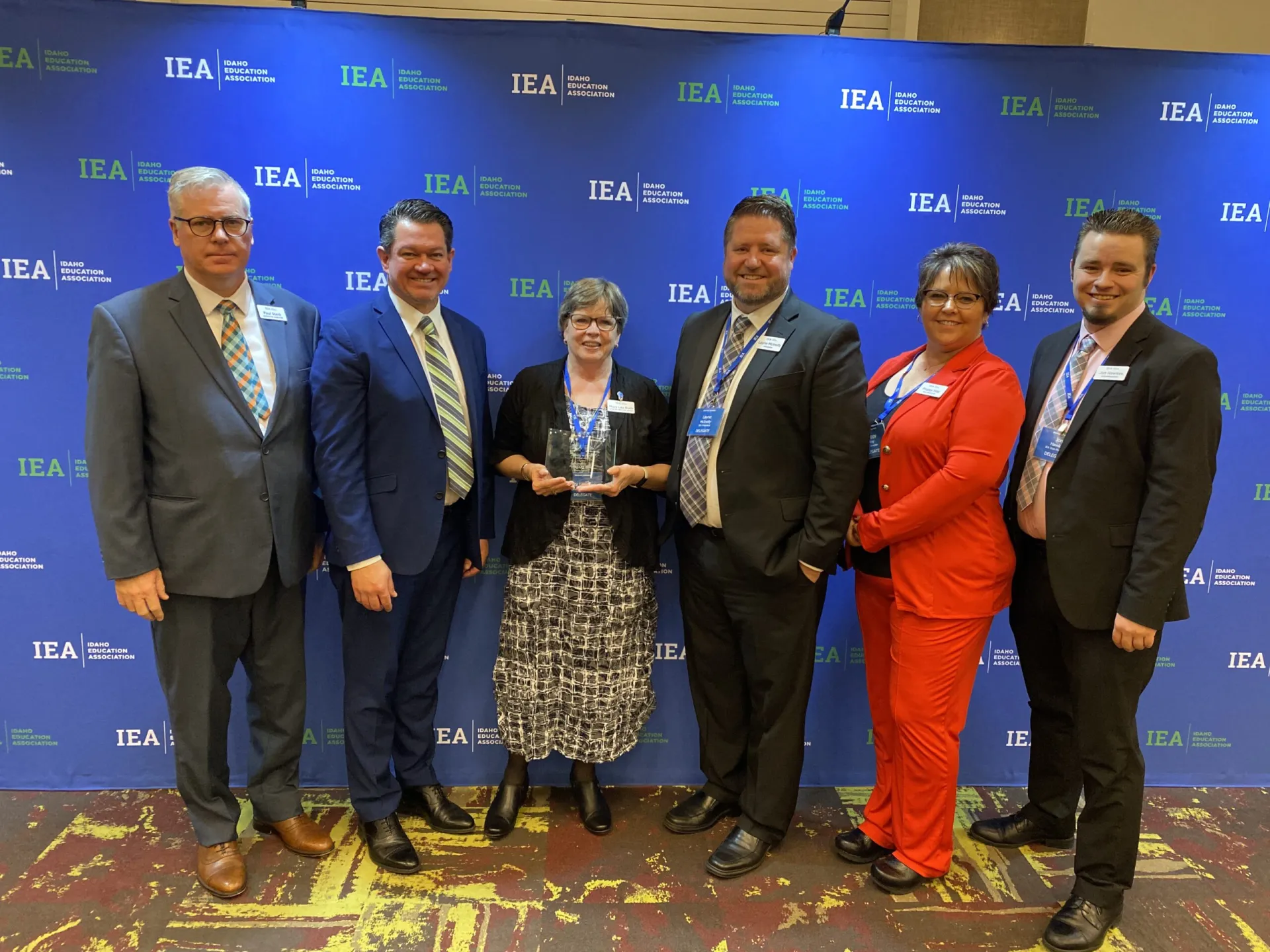 A woman in a black sweater holds an award surrounded by other people