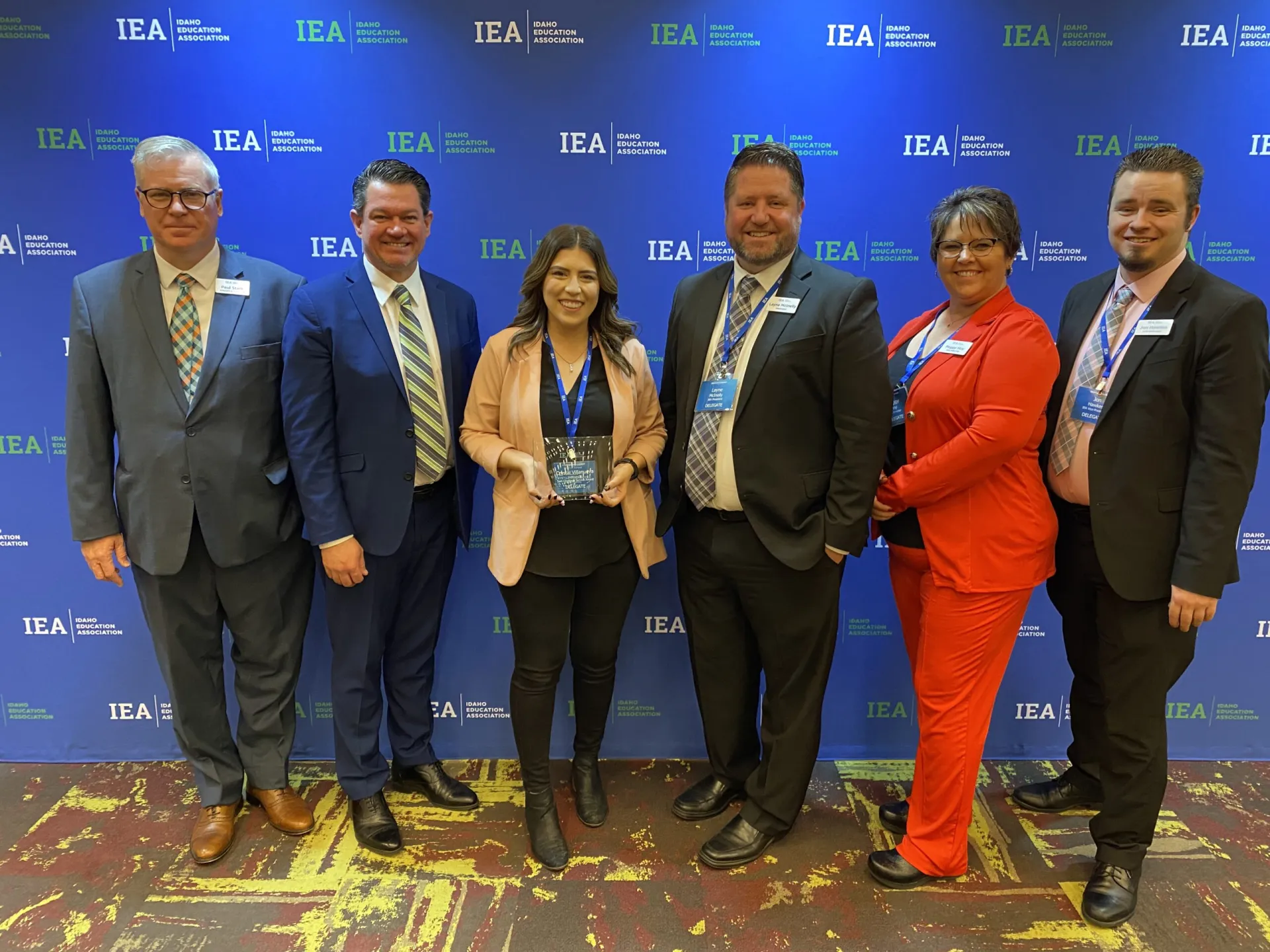 A woman wearing a tan blazer holds an award while flanked by IEA leadership