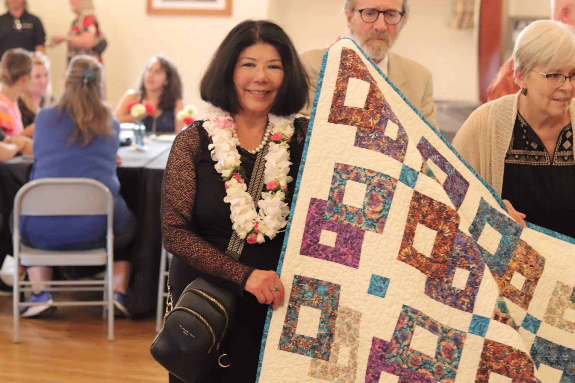 A woman with dark hair holds one end of a quilt and smiles at the camera