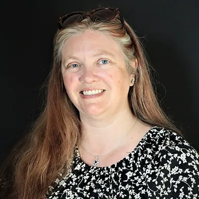 A smiling woman poses against a black background